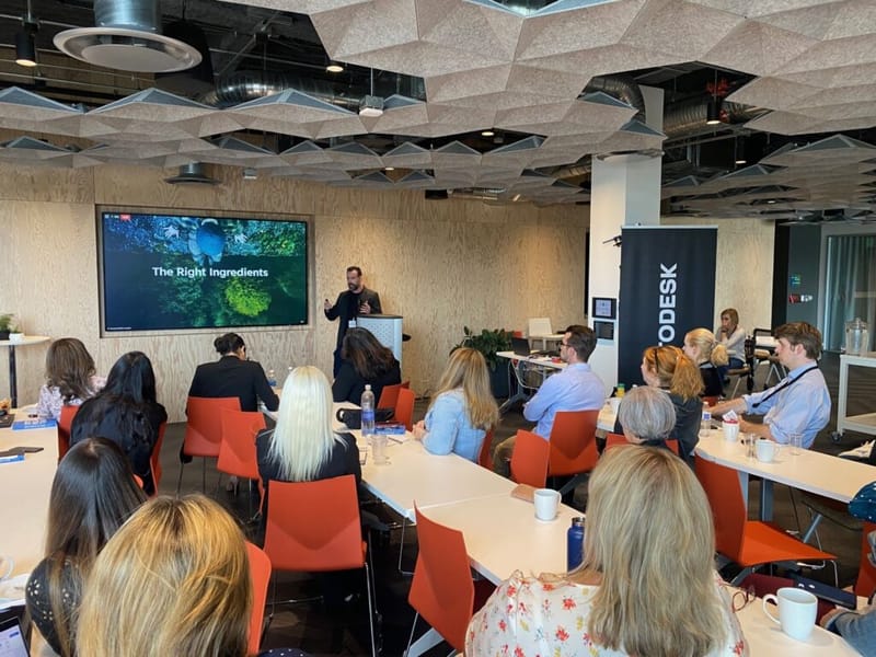 Presenter at Autodesk Partner Summit event beside a slide titled The Right Ingredients, audience seated in orange chairs
